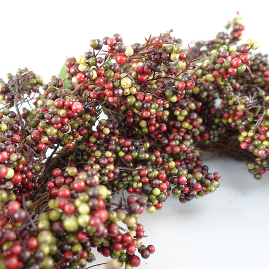A close up of the Plantish 55cm Black Berry Wreath, highlighting the black, green and red berries and green leaves, as well as part of the natural woven ring.
