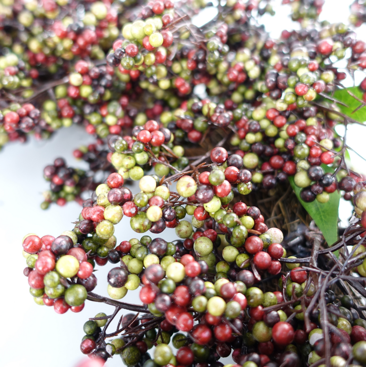 A closer up of the Plantish 55cm Black Berry Wreath, highlighting the black, green and red berries and green leaves, as well as part of the natural woven ring.
