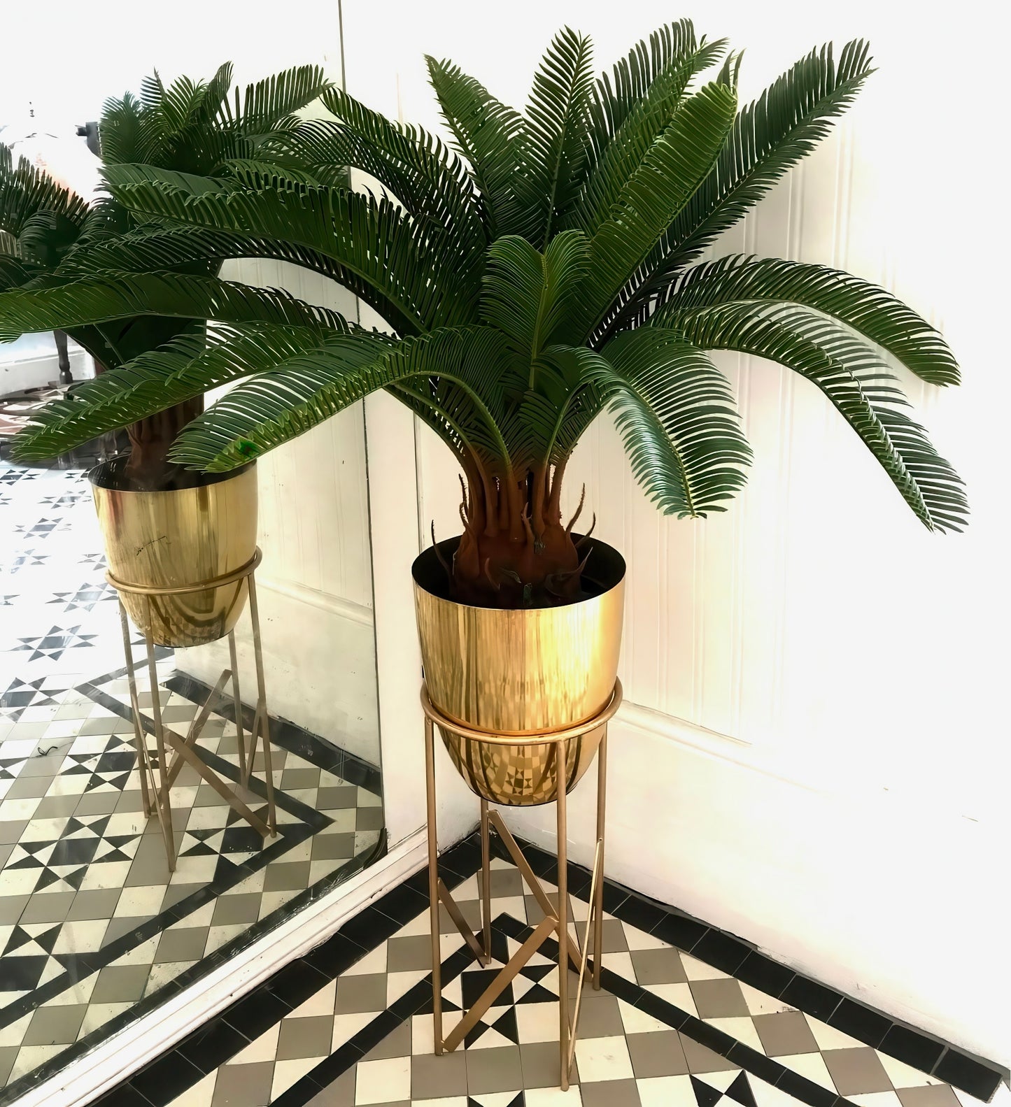Front view of a Plantish artificial cycas palm with lush green fronds, potted in a gold metal pot with a matching stand, placed in the corner of a bright room.