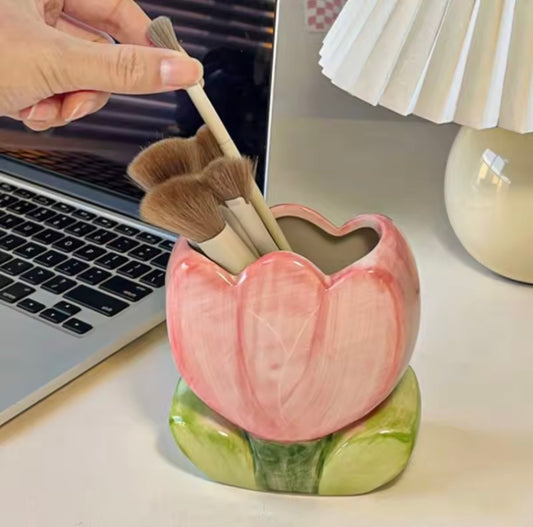 A close up of the Plantish Ceramic Floral Pink Tulip Brush Holder, shown with makeup brushes inside and on a white desk with a laptop and a lamp.