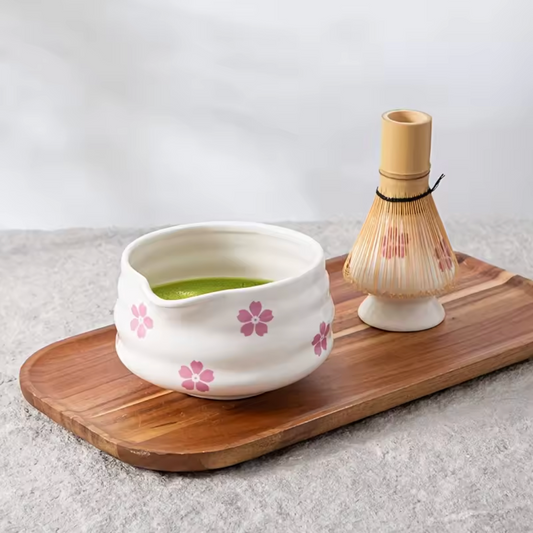 An image of the Plantish Cherry Blossom Matcha Set, showing the bowl full of matcha tea with the whisk and stand, placed on a wooden board.