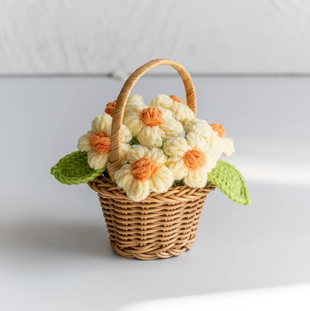 A close up image of the Plantish crocheted flower wicker basket with yellow flowers, placed on a white table with a white wall in the background.