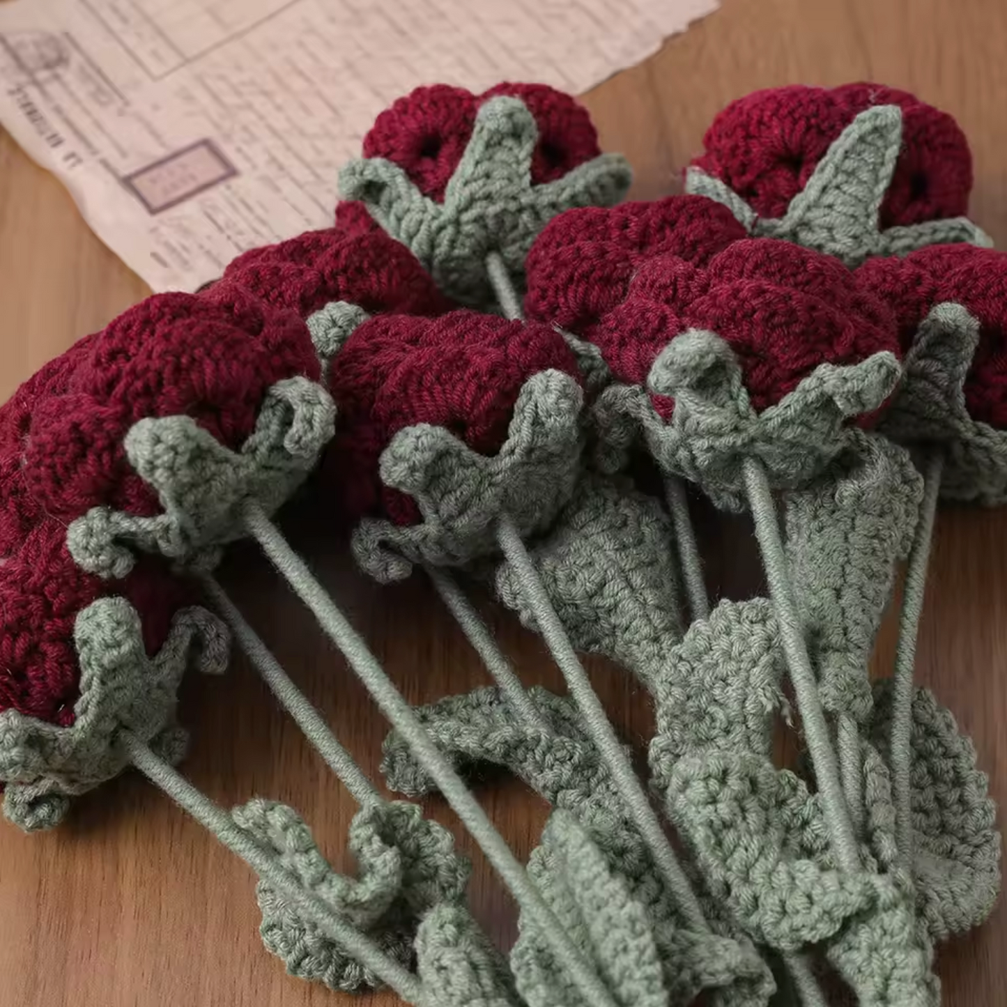 A side view of the Plantish Crocheted Red Roses flowers showing the dark red petals and sage green detailing on the stems and leaves.