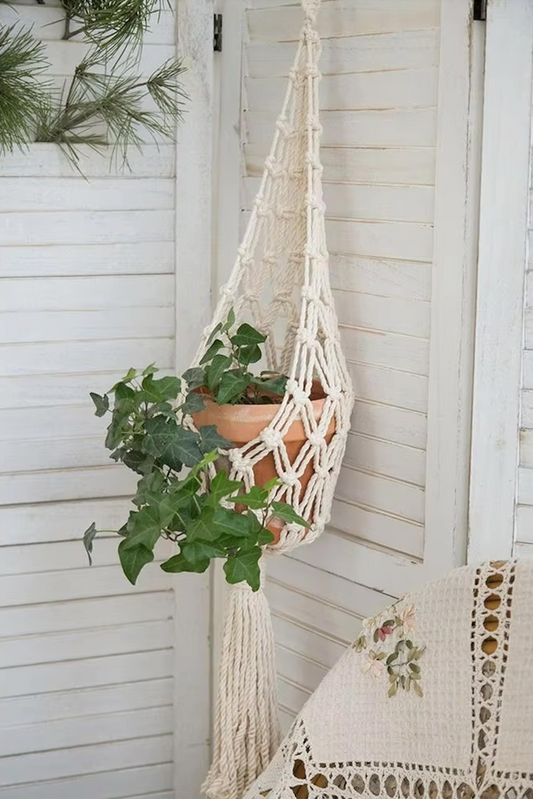 A close up of the Plantish Crosshatch Macrame, which has a terracotta plant pot with a green plant inside. The macrame is suspended outside.