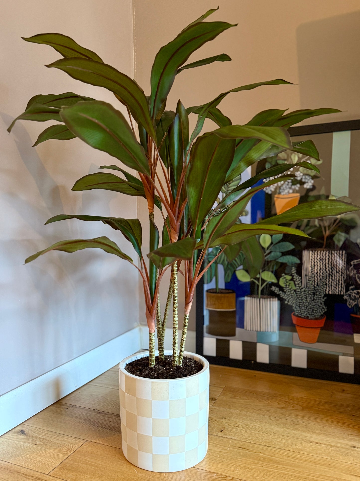 Front view of the realistic Plantish artificial Dracaena, showcasing its tall, pointed leaves and lifelike stems, potted in a white and yellow checkered ceramic planter.