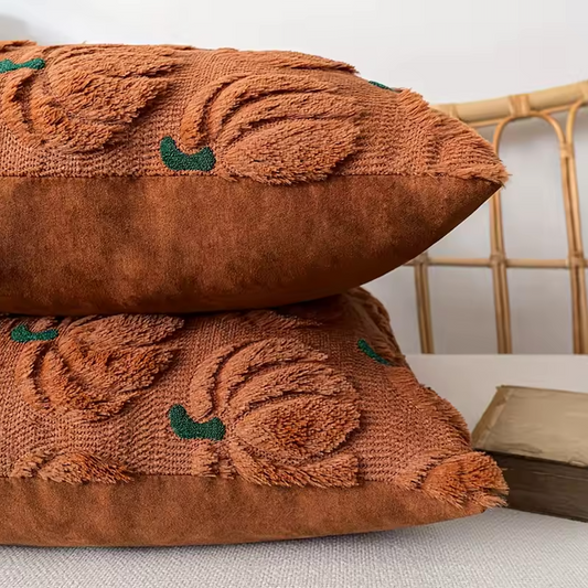 Close up of two brown textured pillows with pumpkin patterns stacked on a light-coloured surface.