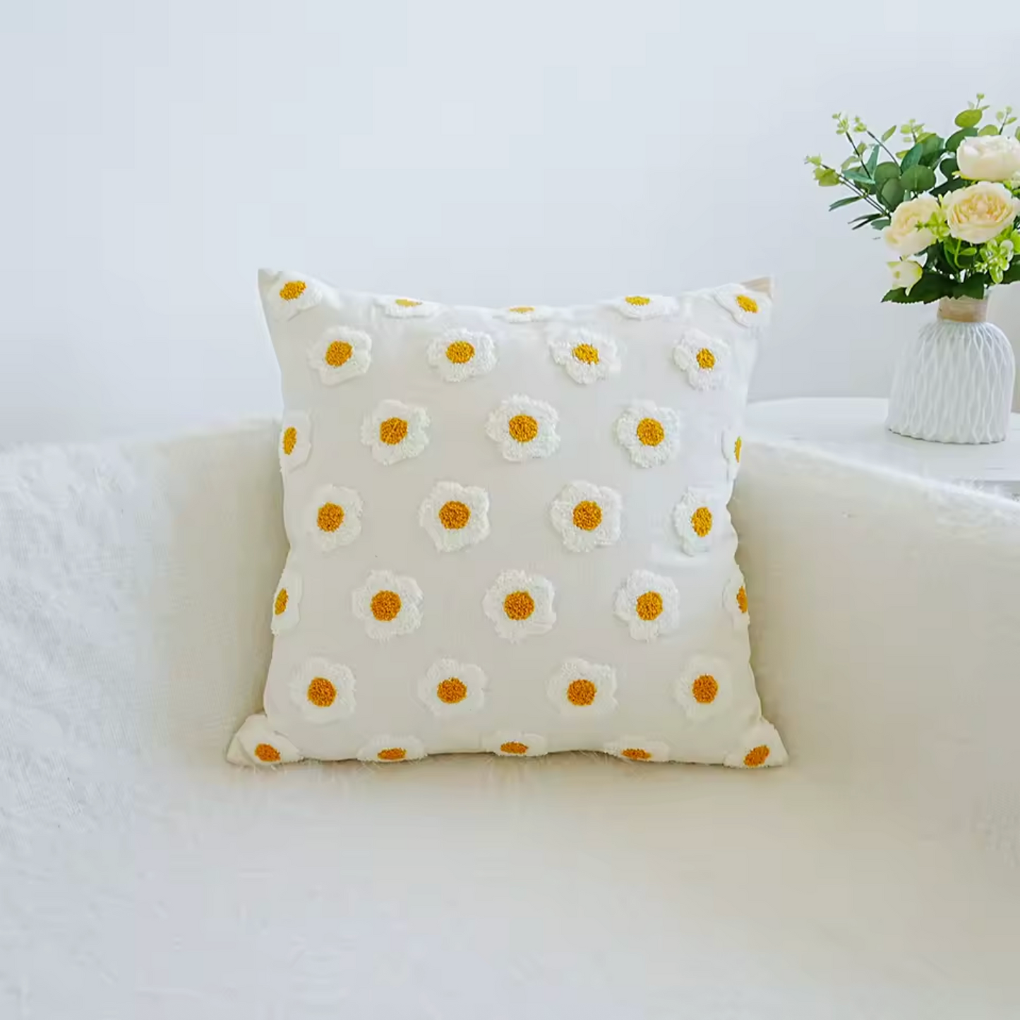 The Square Plantish Embroidered Daisy Cushion Cover in Tiny Daisy design, positioned on a white sofa with a vase of flowers on a table beside it.