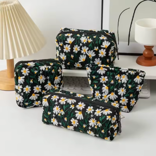 The Plantish Embroidered Little Daisy Makeup Bag in Black shown in four different shapes,
on a white desk with assorted stationary.