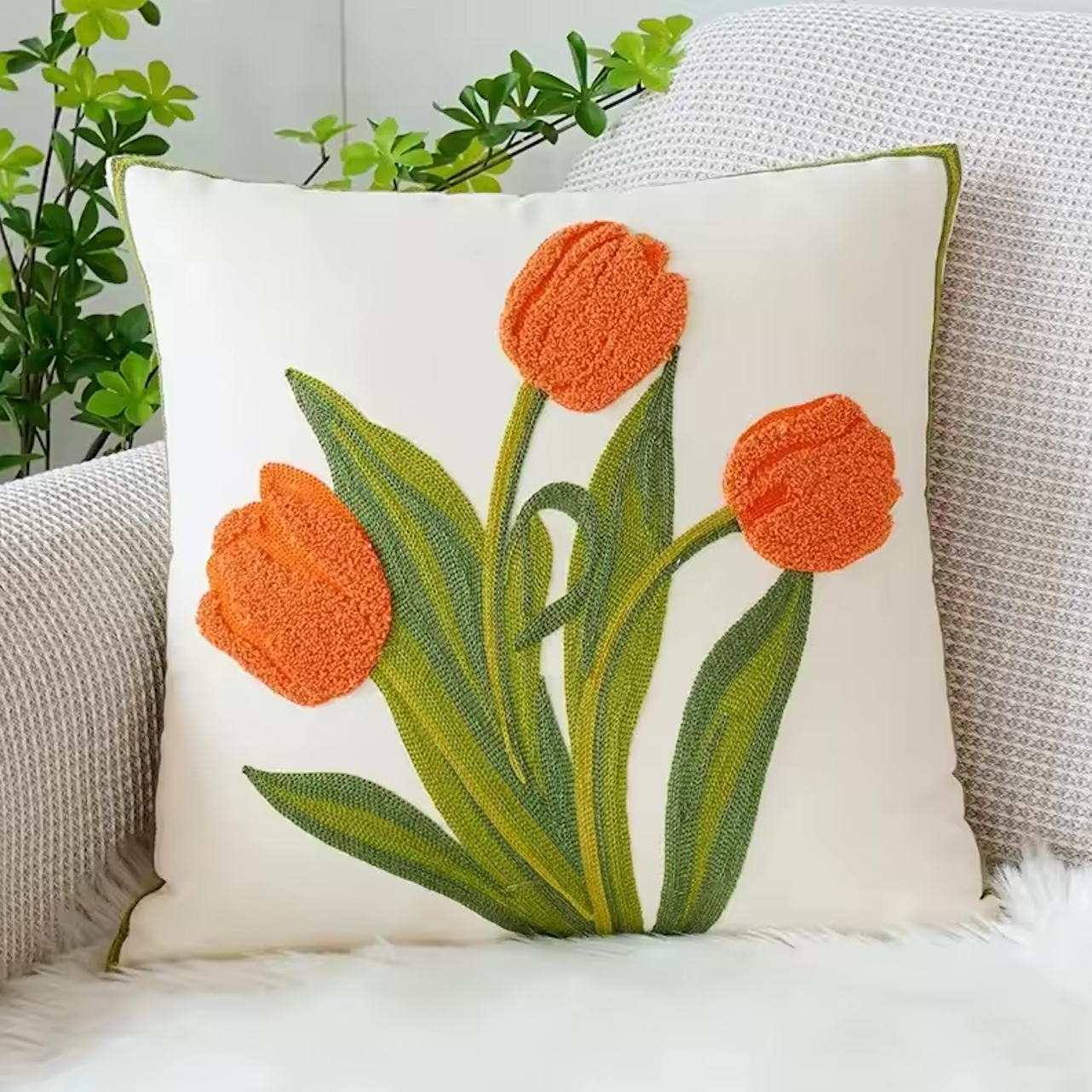 The Plantish Embroidered Tulip Cushion Cover, shown in Orange and positioned on a grey sofa with a green plant visible in the corner.