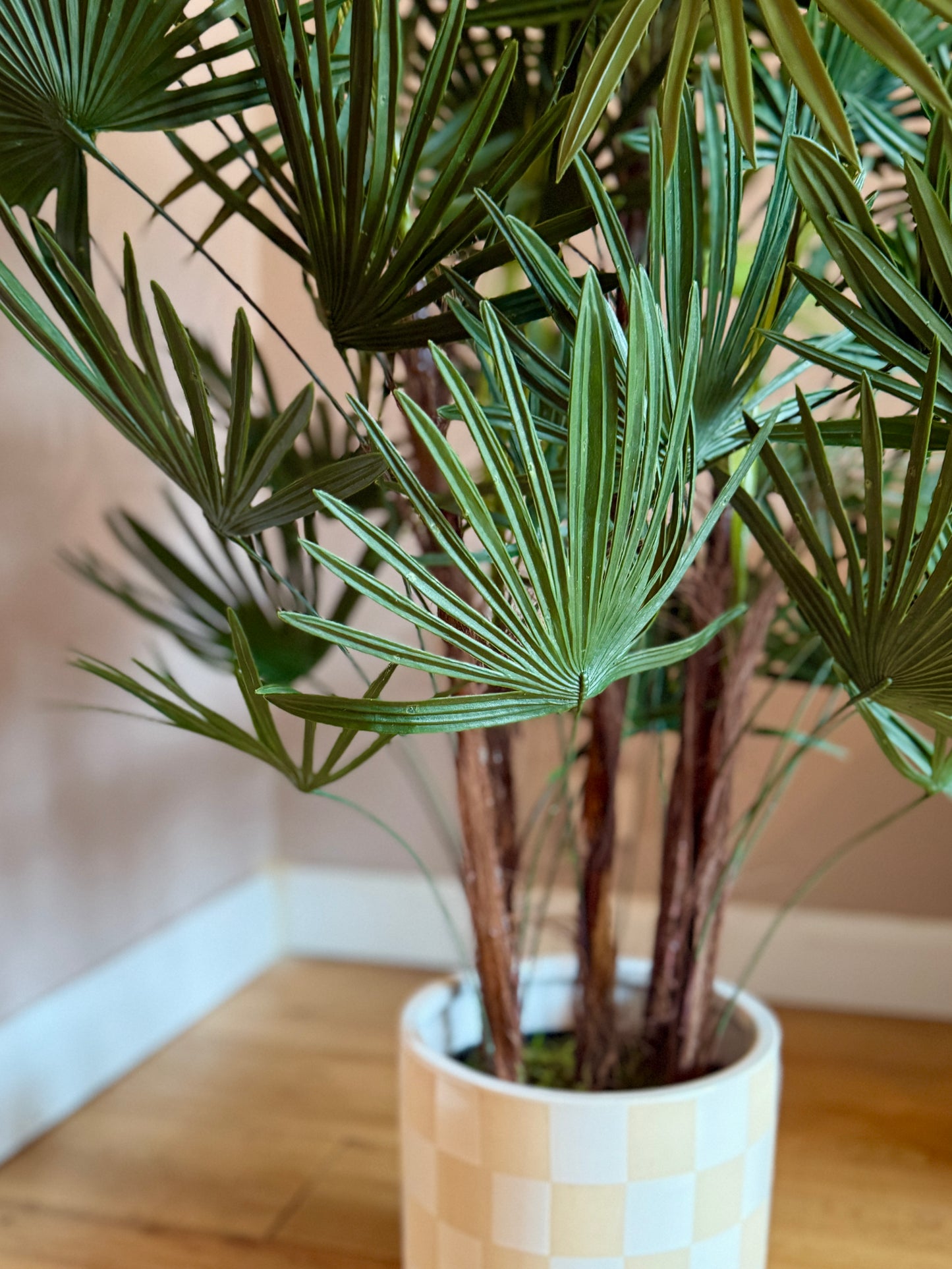 Back view of a Plantish artificial fan palm, showcasing the rich green leaves and the natural bark detail on the stems, in a chequered ceramic pot.