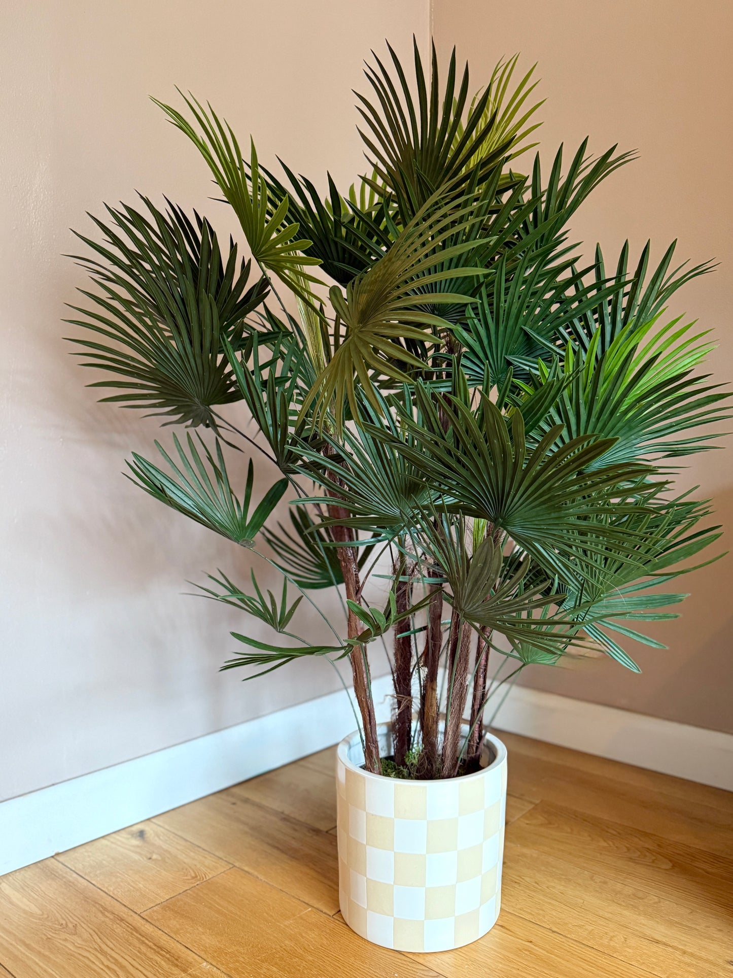 Front view of a Plantish artificial fan palm with vivd green leaves, featuring natural bark on the stems, in a chequered pot.