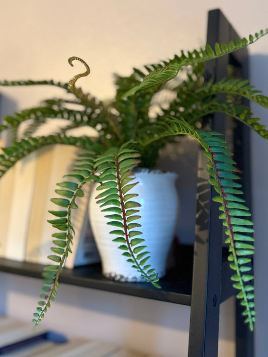 Back view of a Plantish artificial fern, with a soft focus highlighting its vibrant green fronds, in a textured cracked-style ceramic pot.