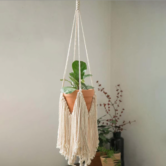Front view of the Plantish Fringe Macrame, which has a terracotta plant pot with a green plant inside. The macrame is suspended in a bedroom.