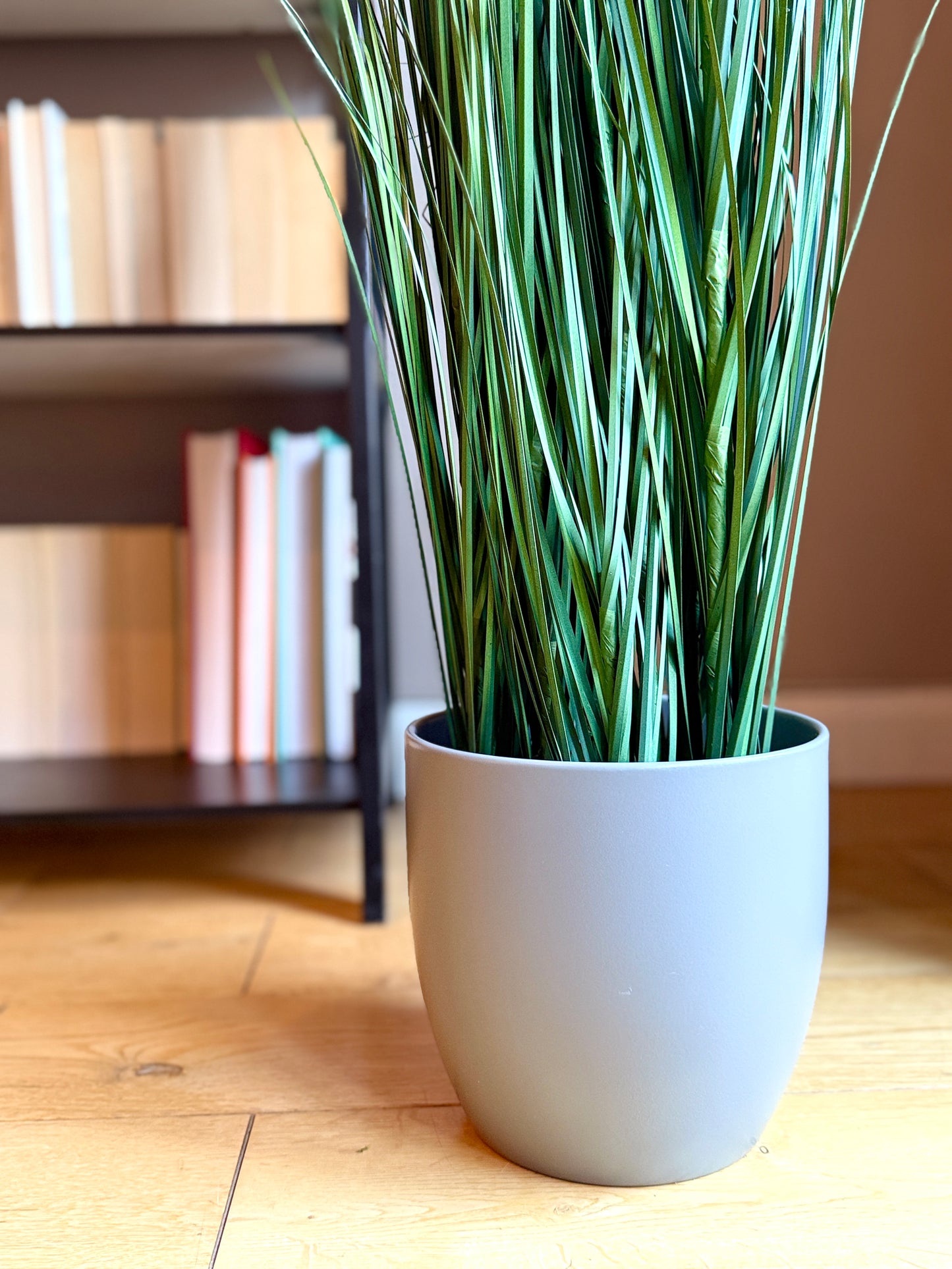 Back view of the Plantish artificial Onion Grass, highlighting the lower portion of the plant and the grey ceramic plant pot.