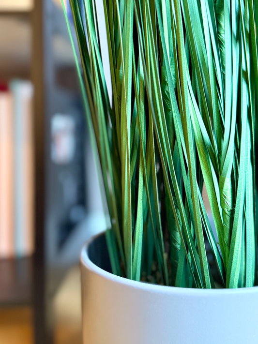 Close up of the base of the Plantish artificial Onion Grass, showcasing the detailed blades and the grey ceramic plant pot.