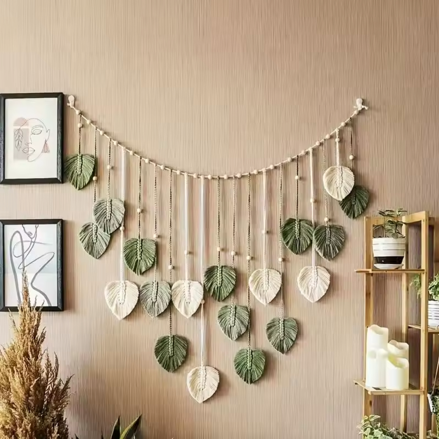 A Plantish Leaf Macrame with green and white leaves and a white string hanging on a textured light brown wall. There are photo frames and a wooden shelf visible.
