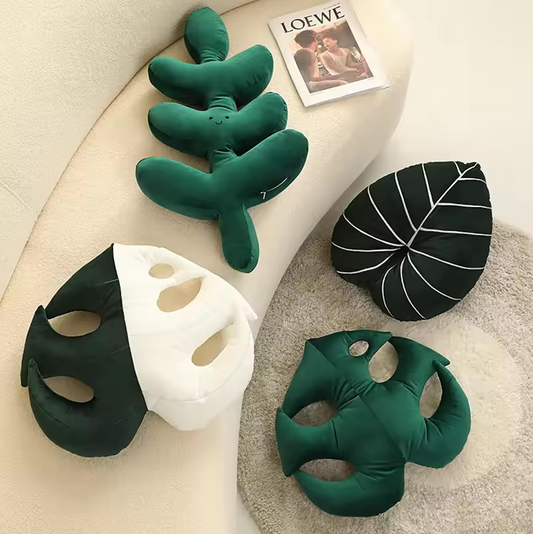 The Plantish Jungle Leaf Cushion in four different designs - two monstera leaf, one fern, one philodendron, Two on a white sofa, two on the floor.