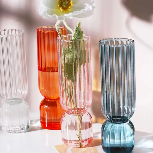 A close up image of the Plantish Little Nordic Vase in four colours - clear, light blue, orange, and pink. They are on a white table.