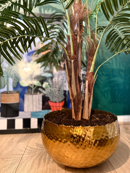 Close up of the Plantish artificial majesty palm, focusing on the intricate green leaves, textured bark on the stem, and real soil inside the hammered metal pot for a lifelike touch.