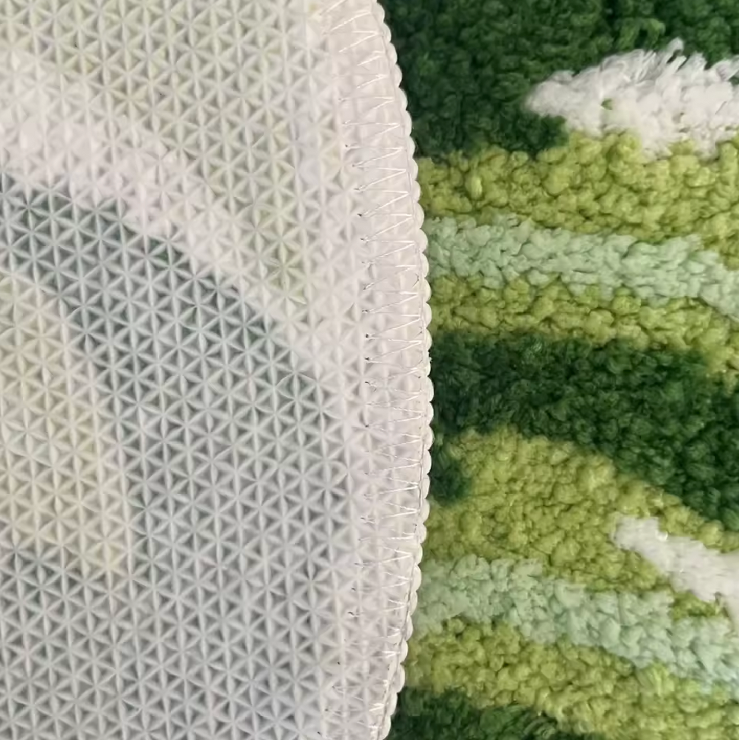A close up of the Plantish Monstera Leaf Tufted Rug, highlighting the non-slip backing and the rich shades of green and white on the design.