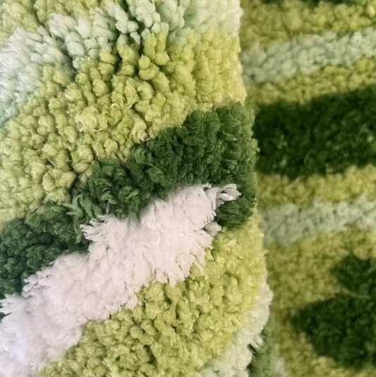 A close up of the Plantish Monstera Leaf Tufted Rug, highlighting the thick and plush fibres and the rich shades of green and white on the design.