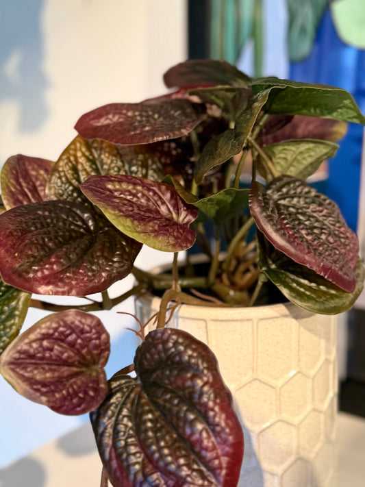 Close up of the Plantish artificial Purple Pothos, highlighting the intricate texture of its vibrant purple and green leaves. The plant is in a white honeycomb ceramic pot.