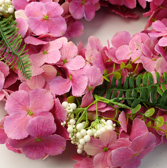 A close up of the Plantish 40cm Pink Cherry Blossom Wreath highlighting the vibrant pink cherry blossom flowers, green fern leaves, and white berries.