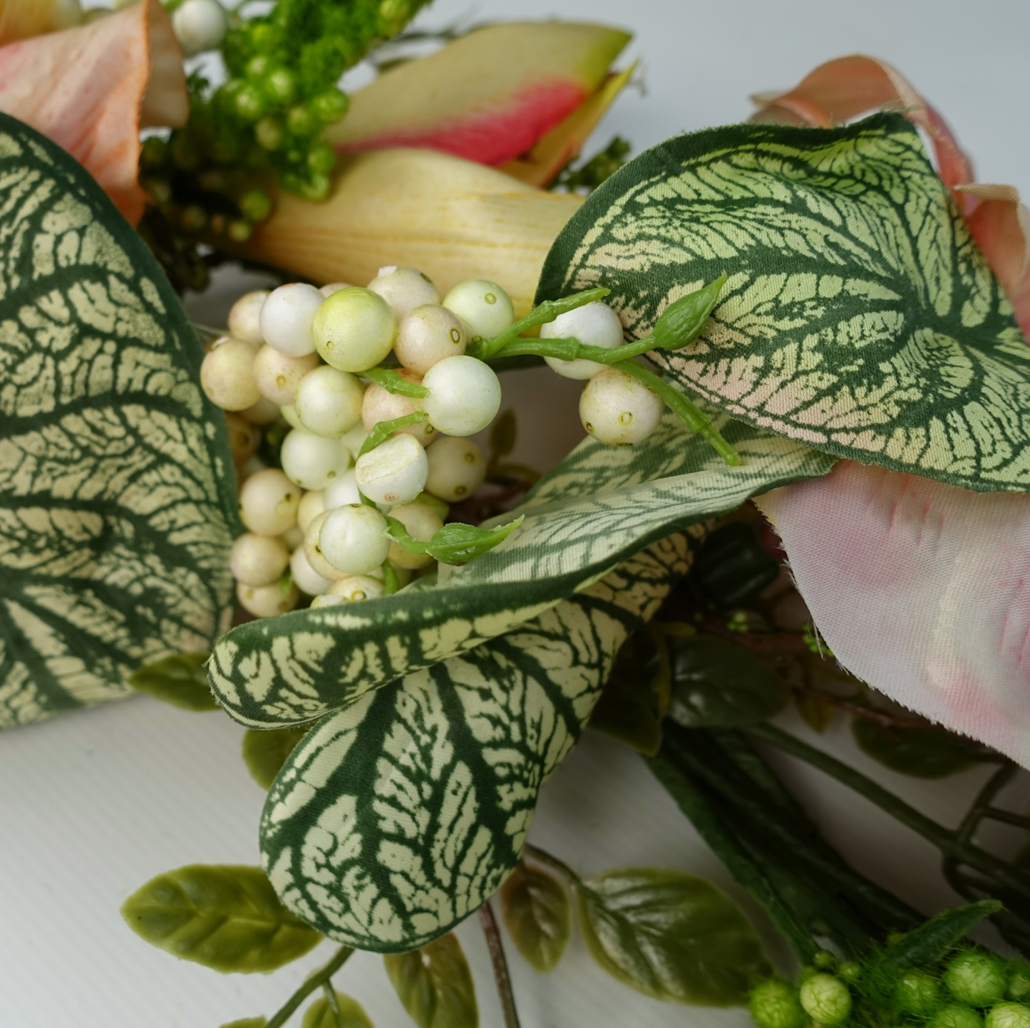A close up of the Plantish 60cm Pink Lily Wreath highlighting the variegated alocasia leaves and white berries.