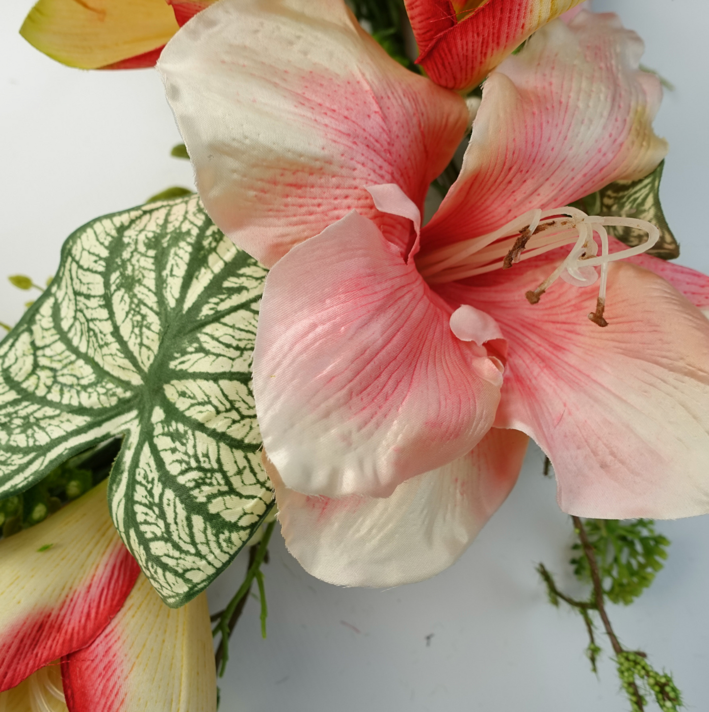 A close up of the Plantish 60cm Pink Lily Wreath highlighting the pink lily flowers and variegated alocasia leaves in detail.