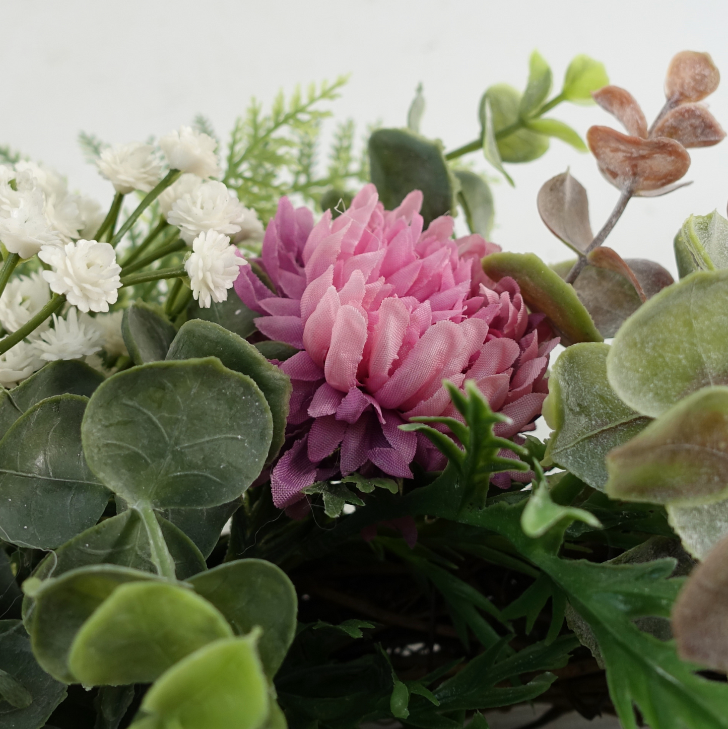A close up of the Plantish 45cm Pink Peony Wreath, highlighting the pink peonies, green leaves and fronds, and small white flowers.