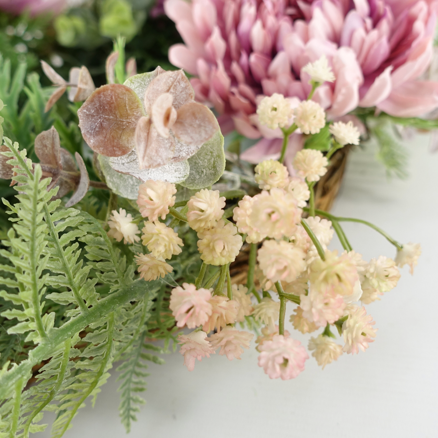 A close up of the Plantish 45cm Pink Peony Wreath, highlighting the pink peonies, green leaves and fronds, and small white flowers.
