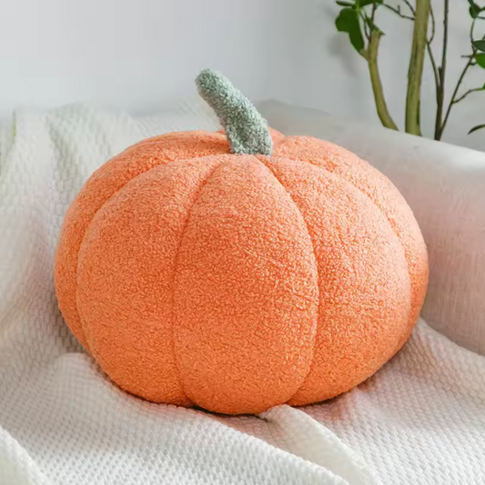 A close up of the Plantish Pumpkin Plush Cushion in Light Orange, shown on a grey sofa with a green plant visible in the background.