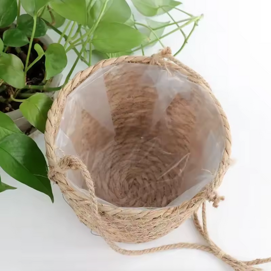 A close up of the Plantish Rattan Hanging Pot showing the plastic lined interior of the pot. There is a green plant next to the pot and both are on a white background.
