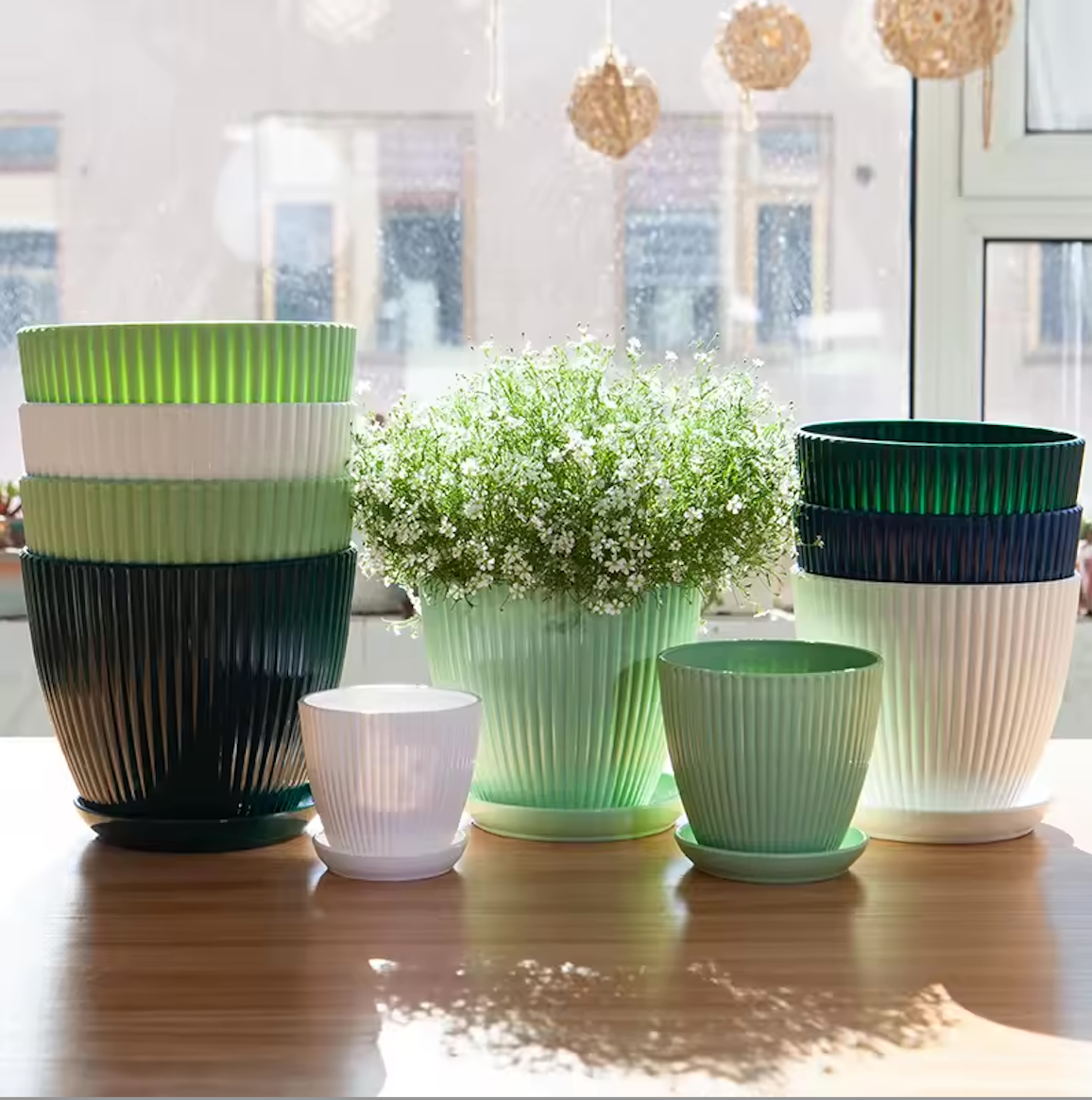 The Plantish Ridged Plastic Planter in various colours and sizes on a wooden table, in front of a window with sun shining through.
