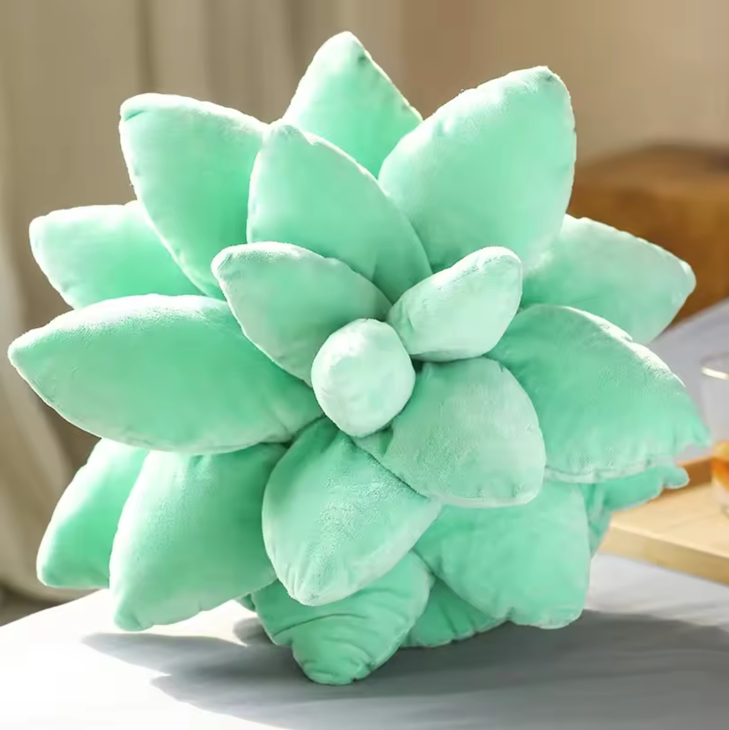 A close up of the top of the Plantish Succulent Plush Cushion in Mint Green, showing the soft leaves, placed on a grey bed with a bedroom in the background.