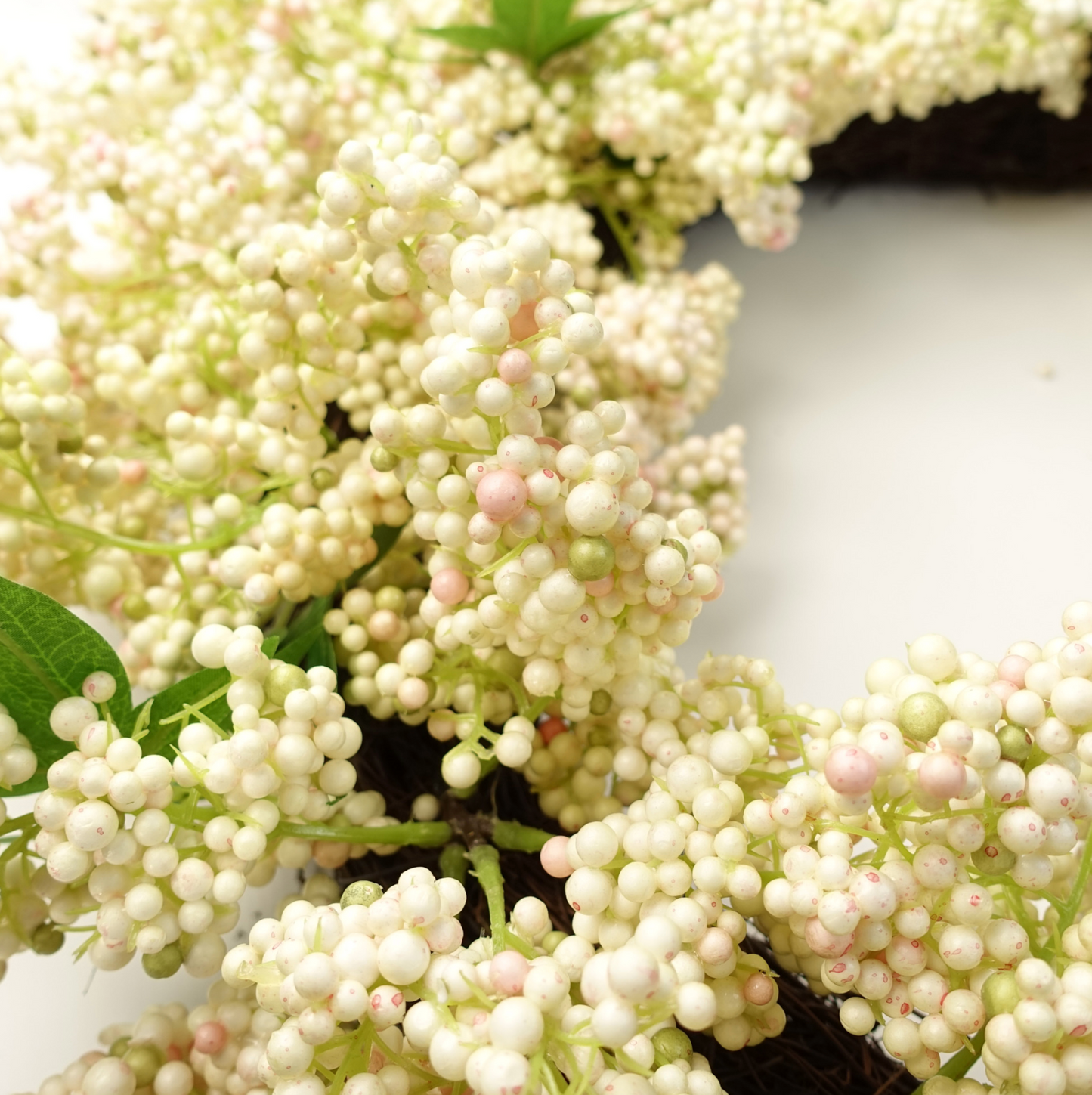 A middle-distance view of the Plantish 55cm White Berry Wreath, showing the write berries, green leaves, and part of the natural woven ring.