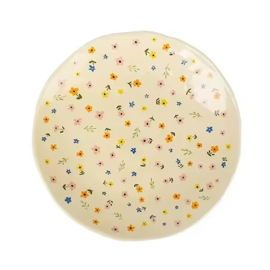 A close up of the Plantish Wildlfower Plate, highlighting the uneven edges and little multicolour flower design. It is on a white background.