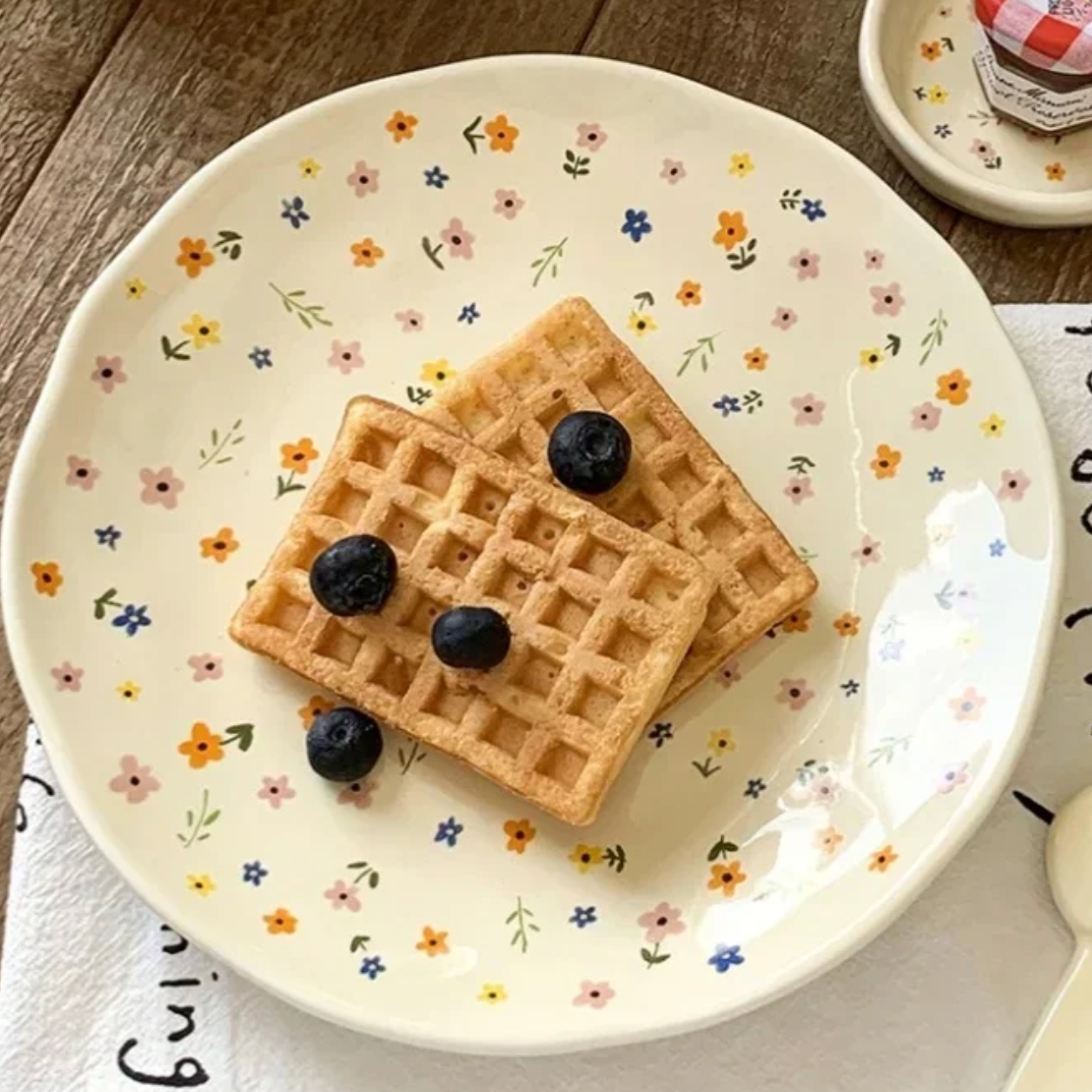 A close up image of the Plantish Wildflower Plate with two waffles and some blueberries on top of it, positioned on a wood table.