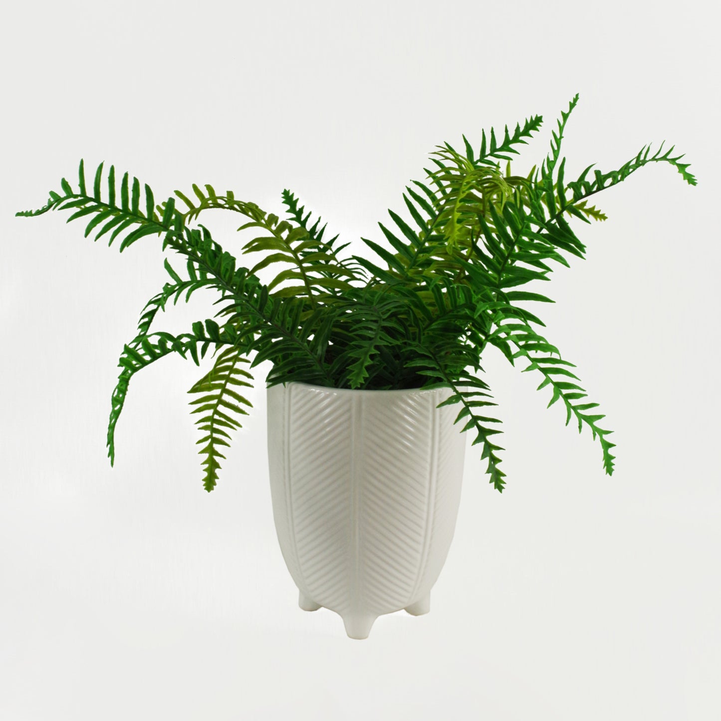 A front view of a white ceramic plant pot with a zig zag herringbone design and small feet with a green artificial fern inside, on a white background.