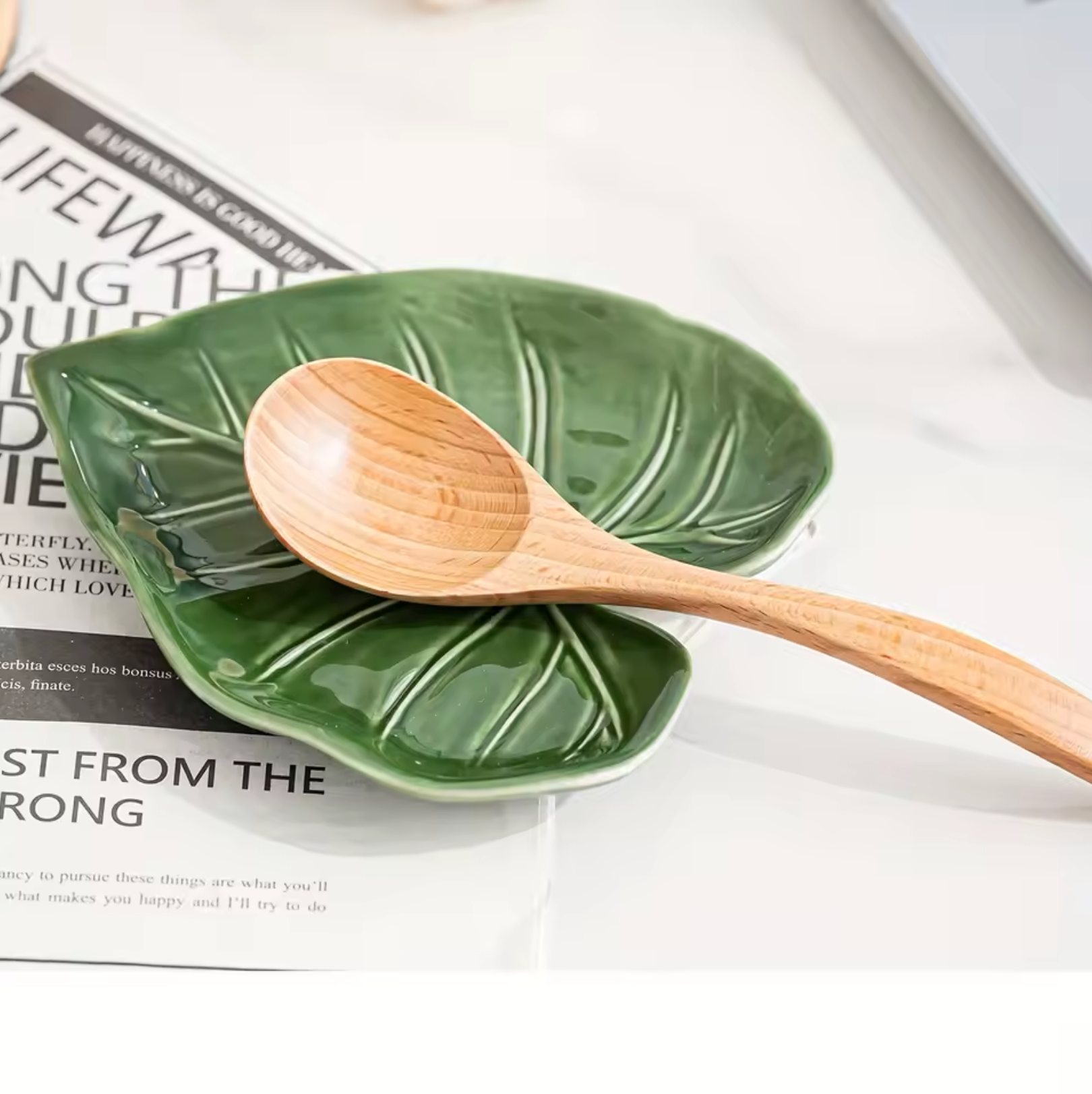The Plantish Alocasia Leaf Ceramic Dish  with a wooden spoon resting on it, on a newspaper background.