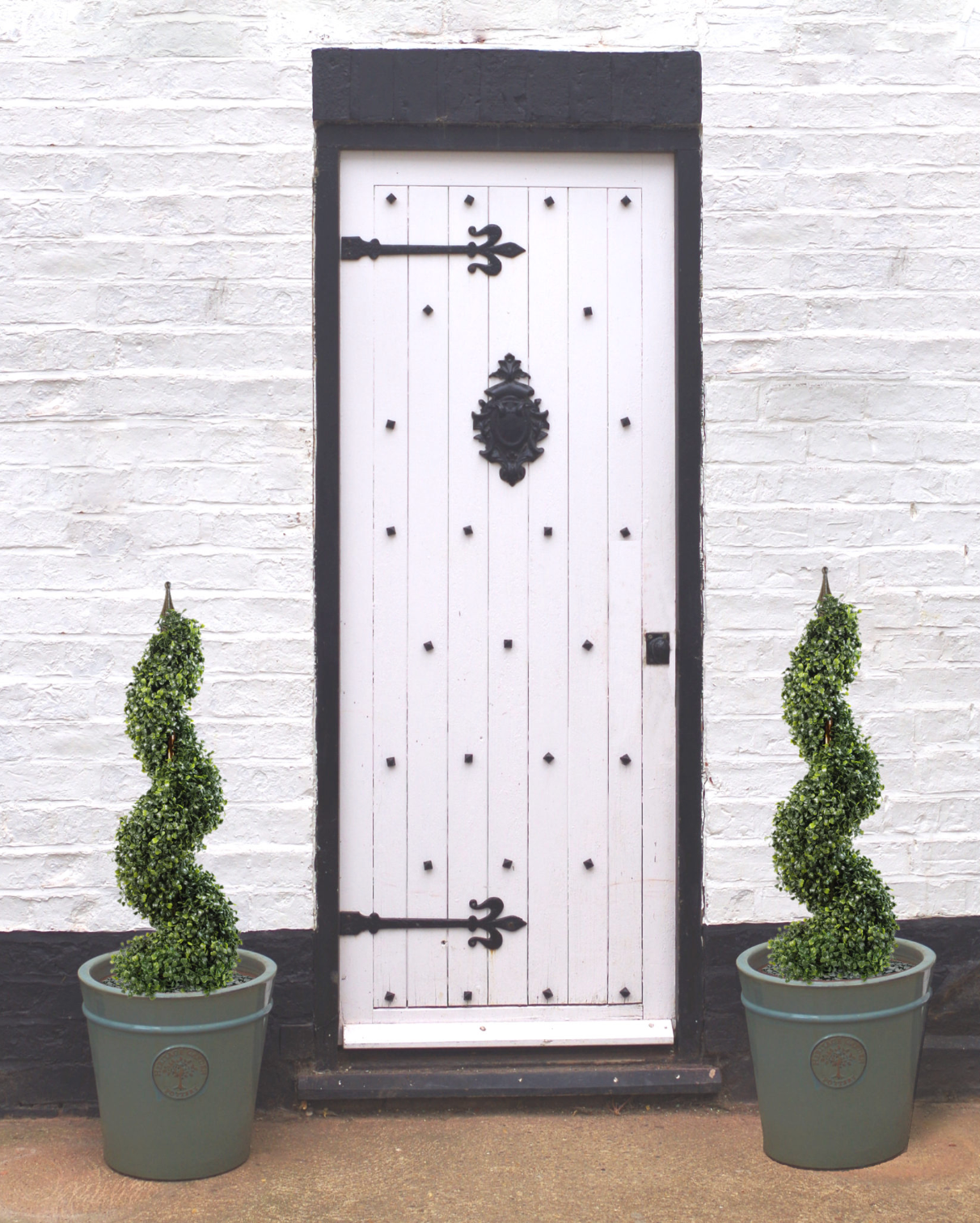 The Plantish Artificial Boxwood Topiary Trees, shown in ceramic pots either side of a white exterior door. The green spiral design is highlighted.