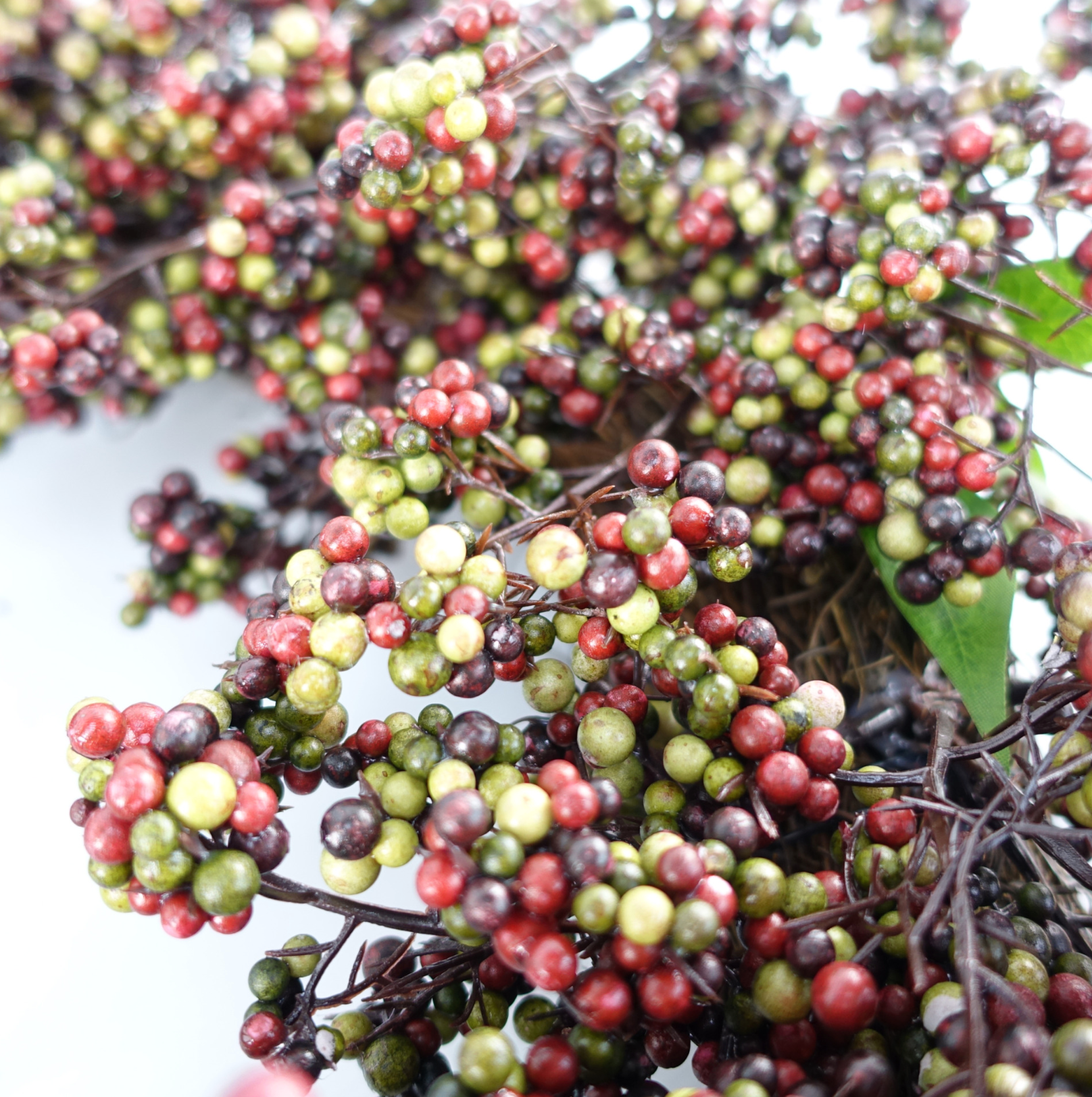 A closer up of the Plantish 55cm Black Berry Wreath, highlighting the black, green and red berries and green leaves, as well as part of the natural woven ring.