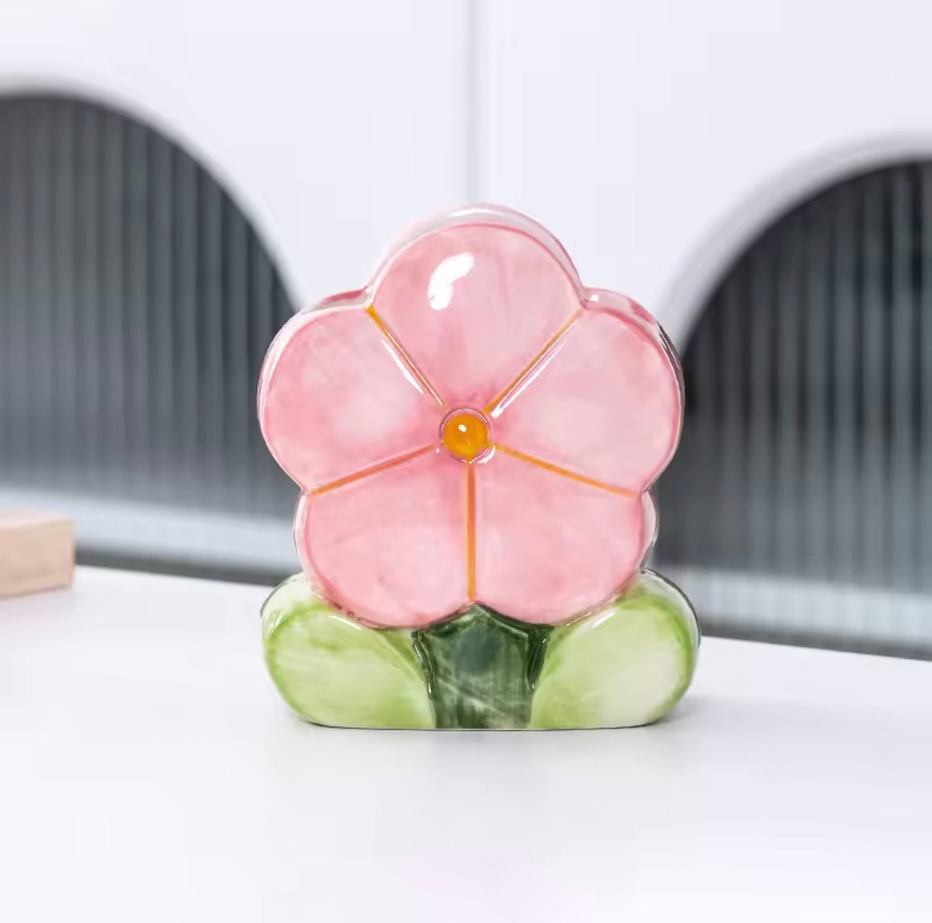 A close up of the Plantish Ceramic Floral Pink Daisy Brush Holder, shown on a white desk and highlighting the detail of the flower. 

