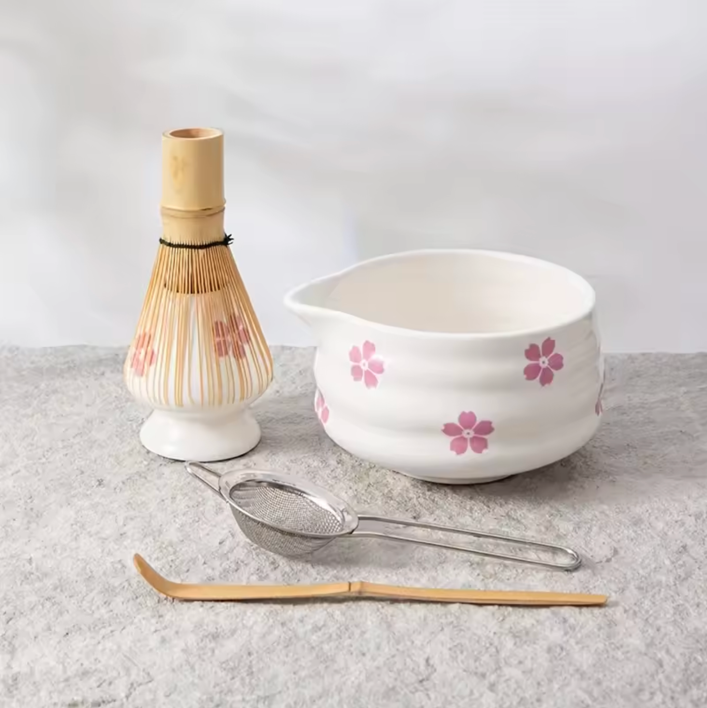 An image of the Plantish Cherry Blossom Matcha Set, showing the matcha whisk & stand, bowl, sieve, and spoon. The bowl and spoon have a cherry blossom design.