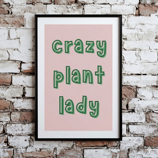 A Plantish print of the phrase "Crazy Plant Lady" in a green font with pink background, shown hanging on a brick wall.