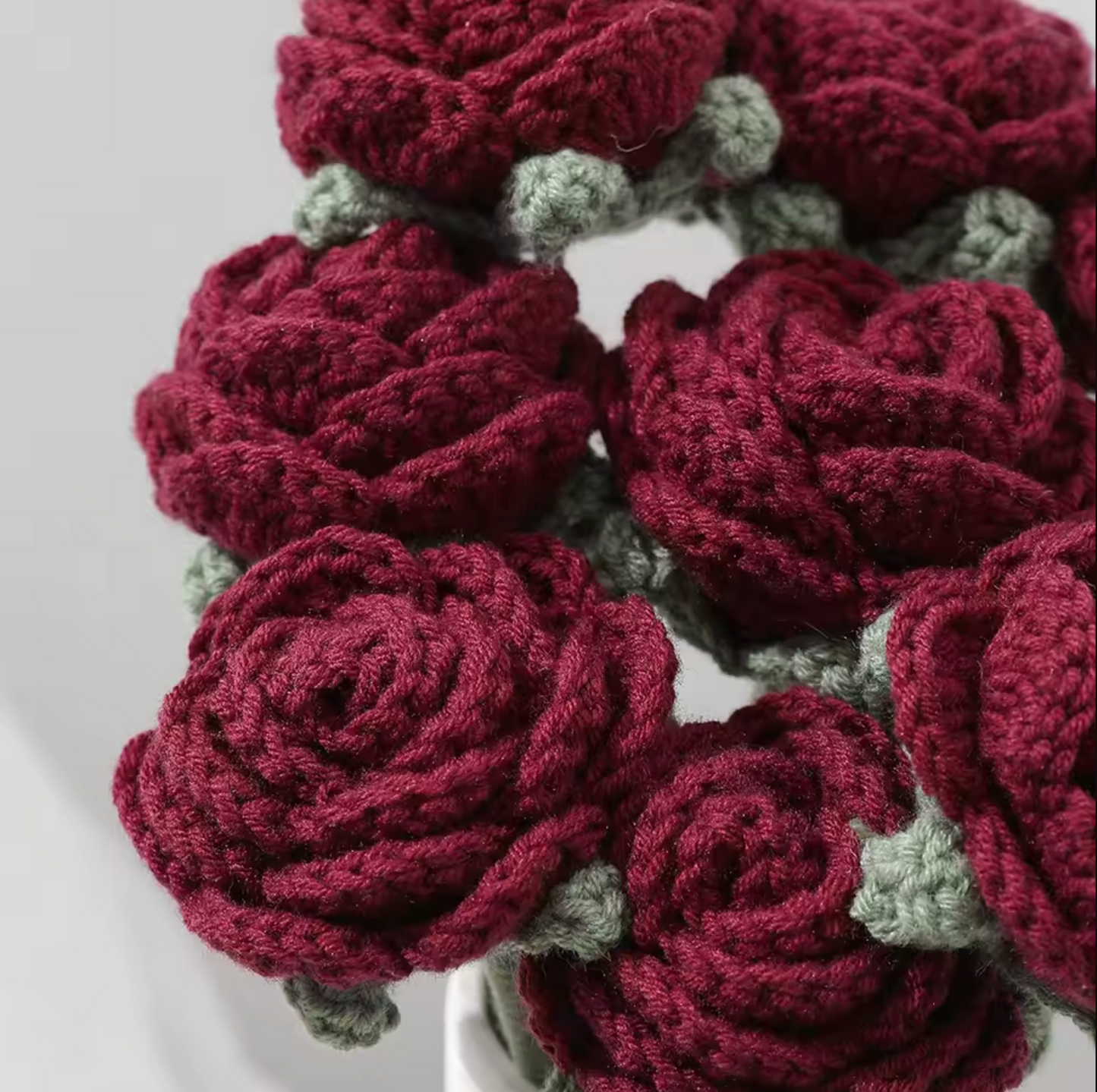 A close up of the Plantish Crocheted Red Roses flowers, highlighting the dark red petals and sage green detailing. 