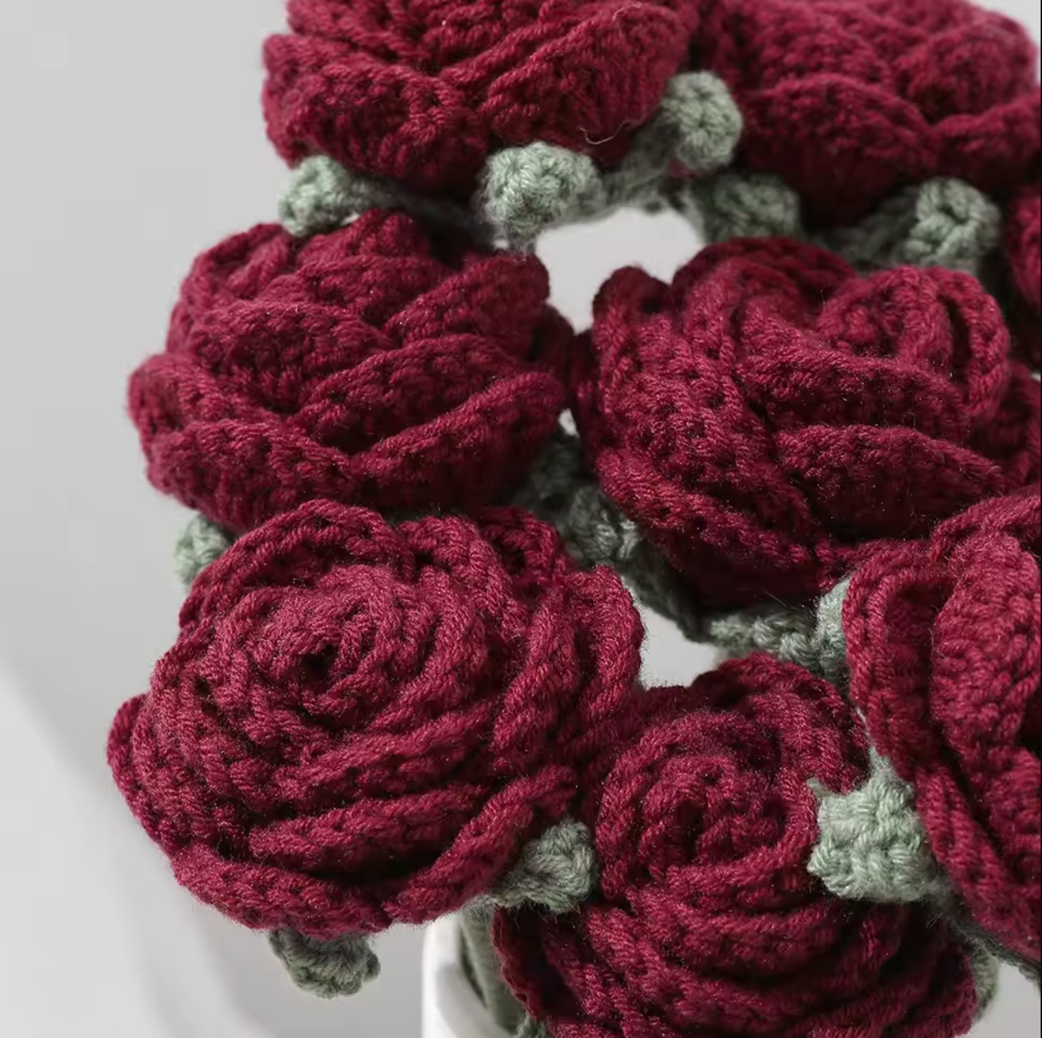 A close up of the Plantish Crocheted Red Roses flowers, highlighting the dark red petals and sage green detailing. 
