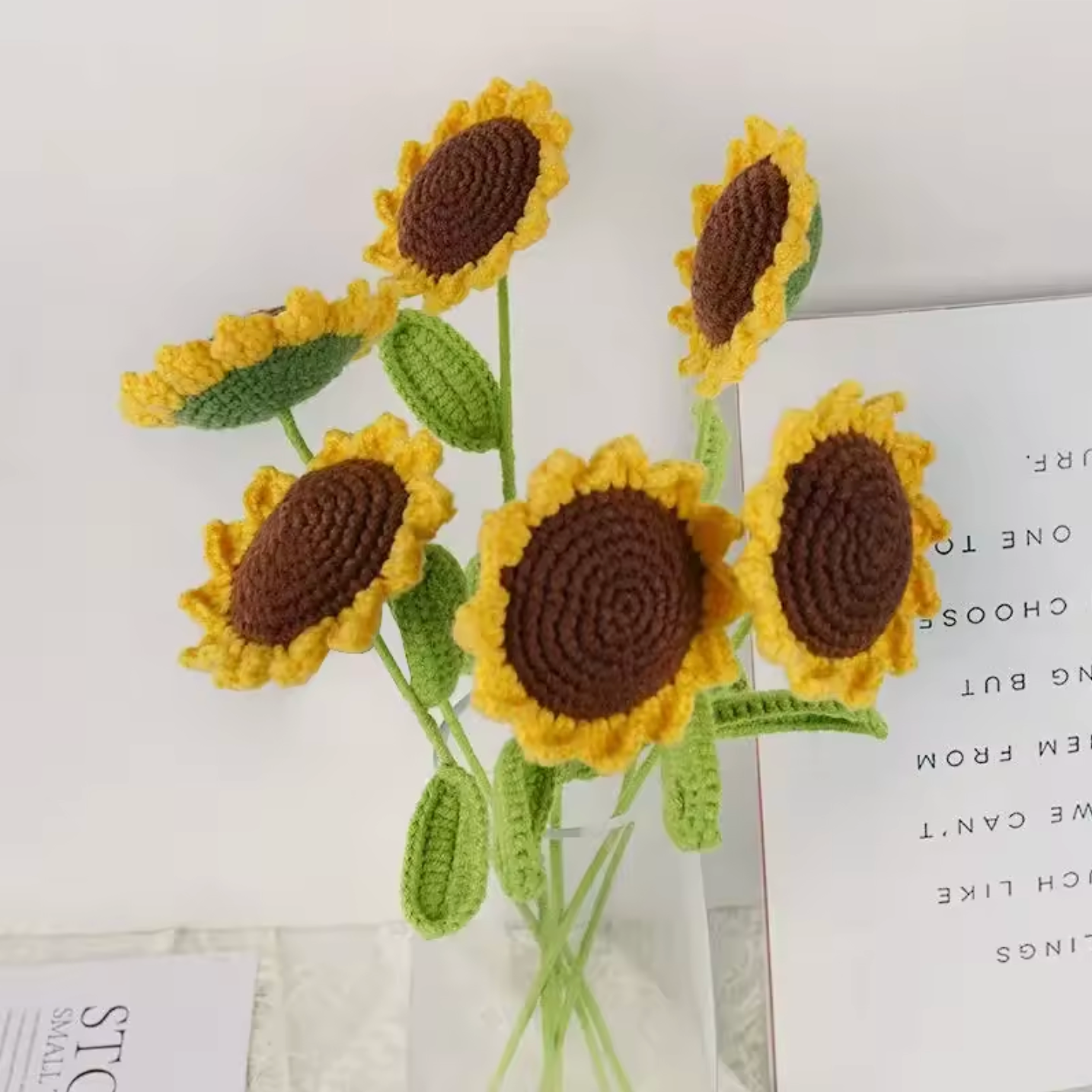 An image of six Plantish Crocheted Sunflowers styled in a clear glass vase. The flowers are shown from several angles. 