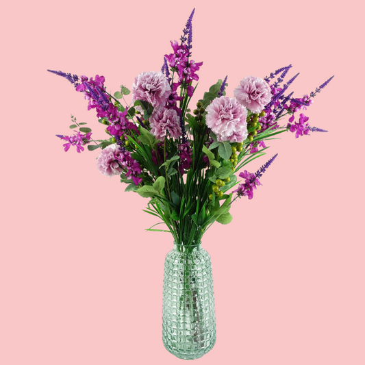 Side view of the Plantish Cube Vase, made of teal coloured glass with a textured cube design. Shown with artificial purple flowers inside and on a pink background.
