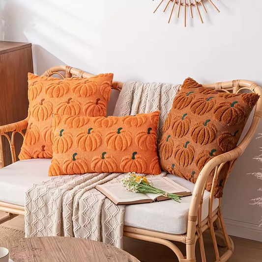 Decorative pillows with embroidered pumpkin pattern on a wicker chair with a blanket and flowers.